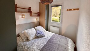 Een slaapkamer met een bed, beddengoed met een patroon, een hanglamp en een raam met uitzicht op groen.