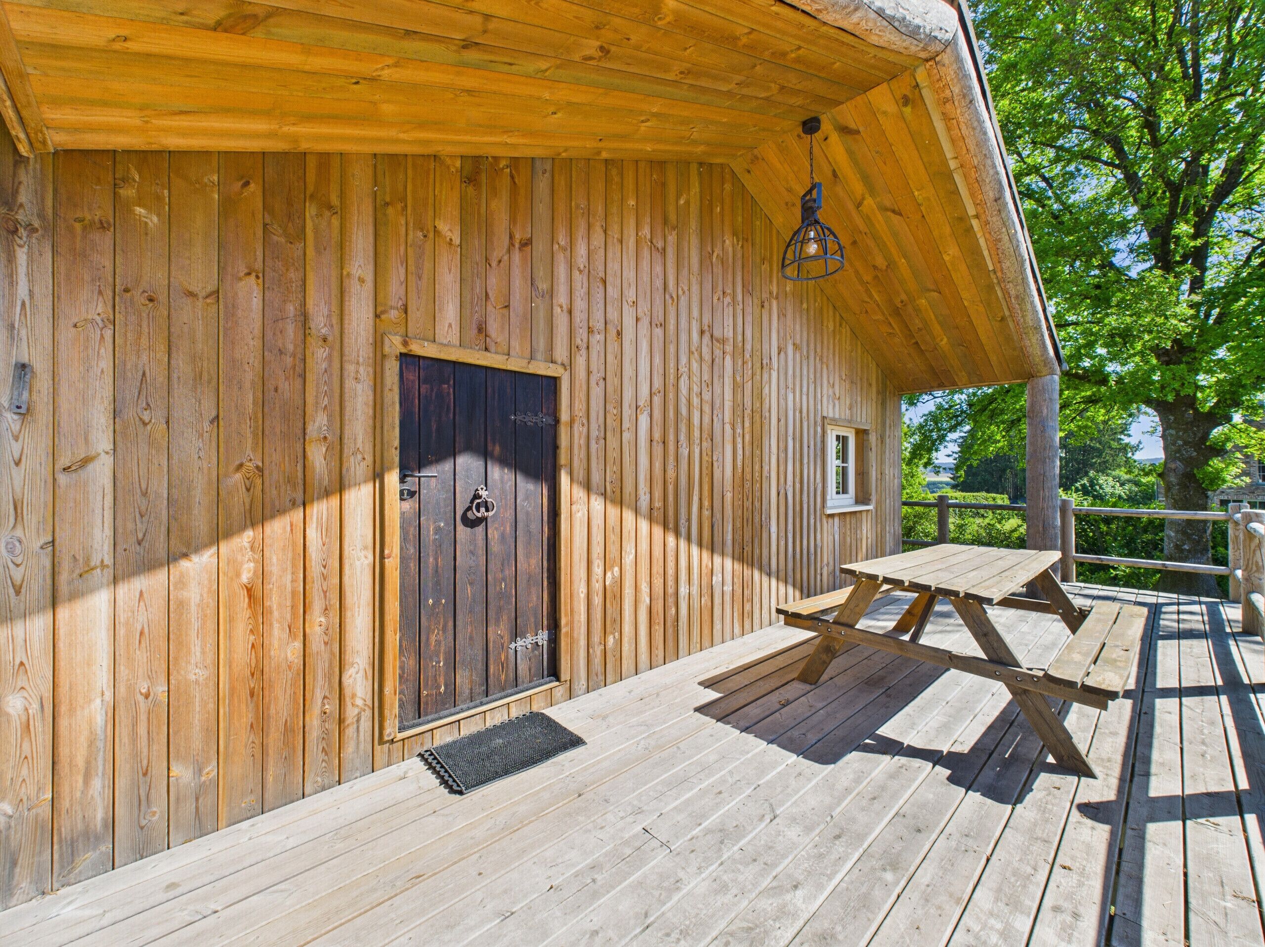 Eine Holzhütte mit Tür, einem kleinen Fenster und einem Picknicktisch auf einer Terrasse.