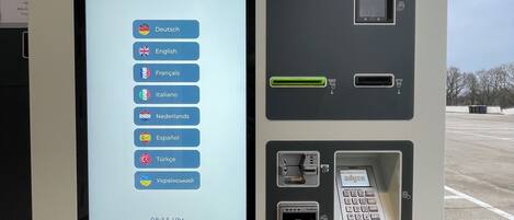 A digital kiosk with a screen displaying a hotel booking interface in multiple languages, a card reader, and a keypad.