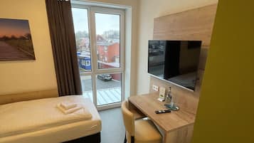 Hotelkamer met een bed, bureau, stoel, televisie en raam met uitzicht op gebouwen en een auto.
