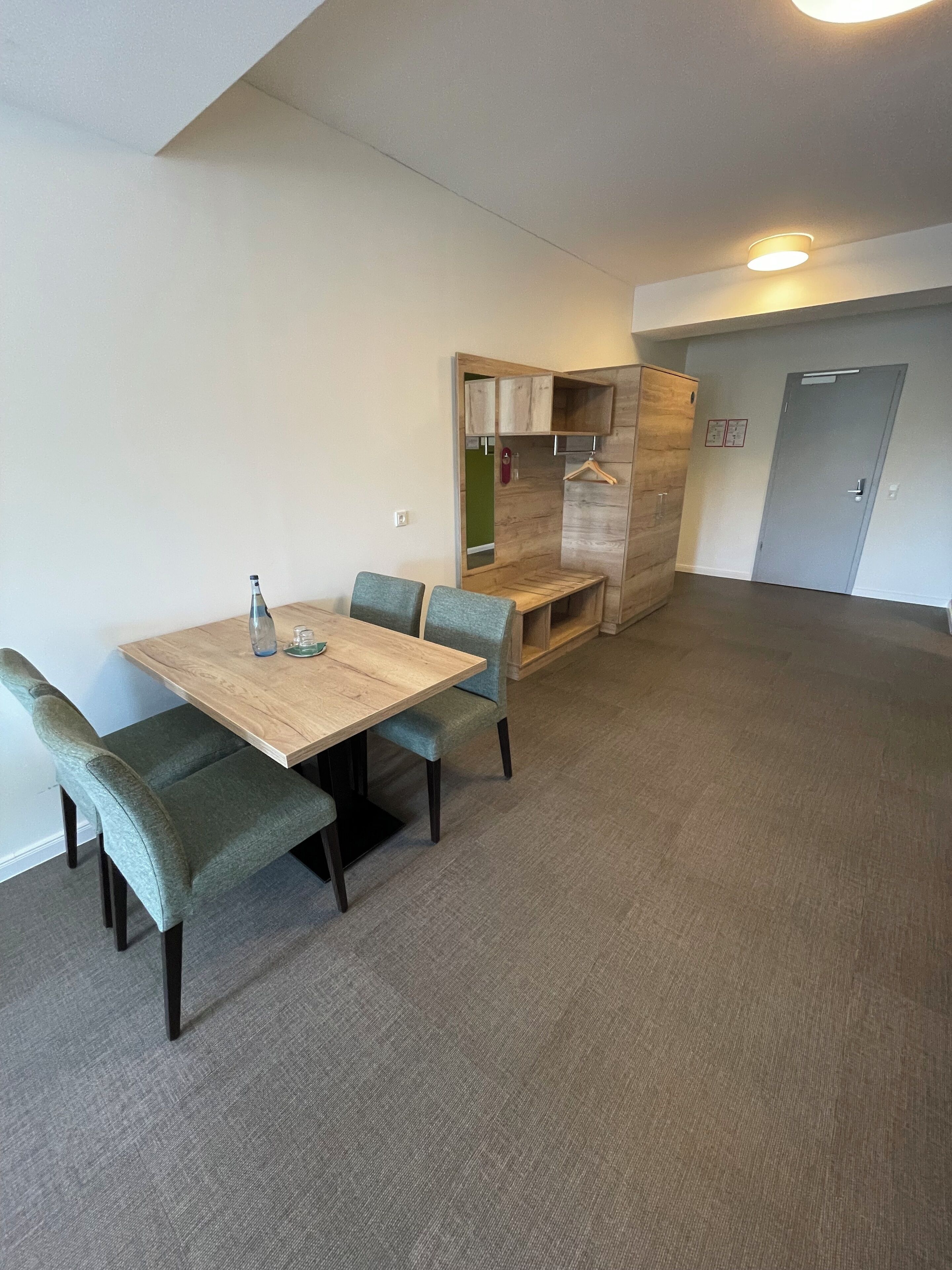 A room with a wooden table and four chairs, a bench, a coat rack, and a door.
