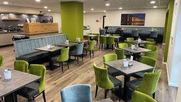 A restaurant with booths and tables, green and blue chairs, and a wooden floor.