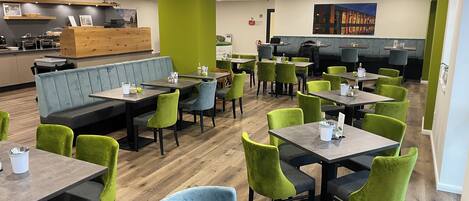A restaurant with booths and tables, green and blue chairs, and a wooden floor.