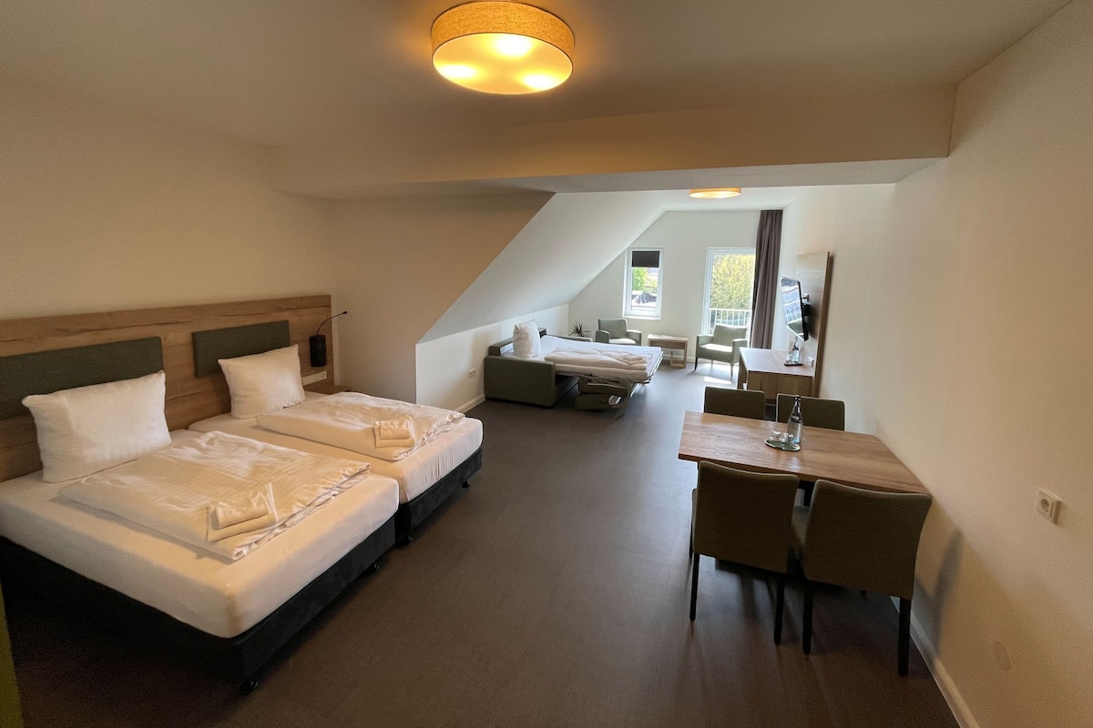 A hotel room with two beds, a dining table, and a small seating area.