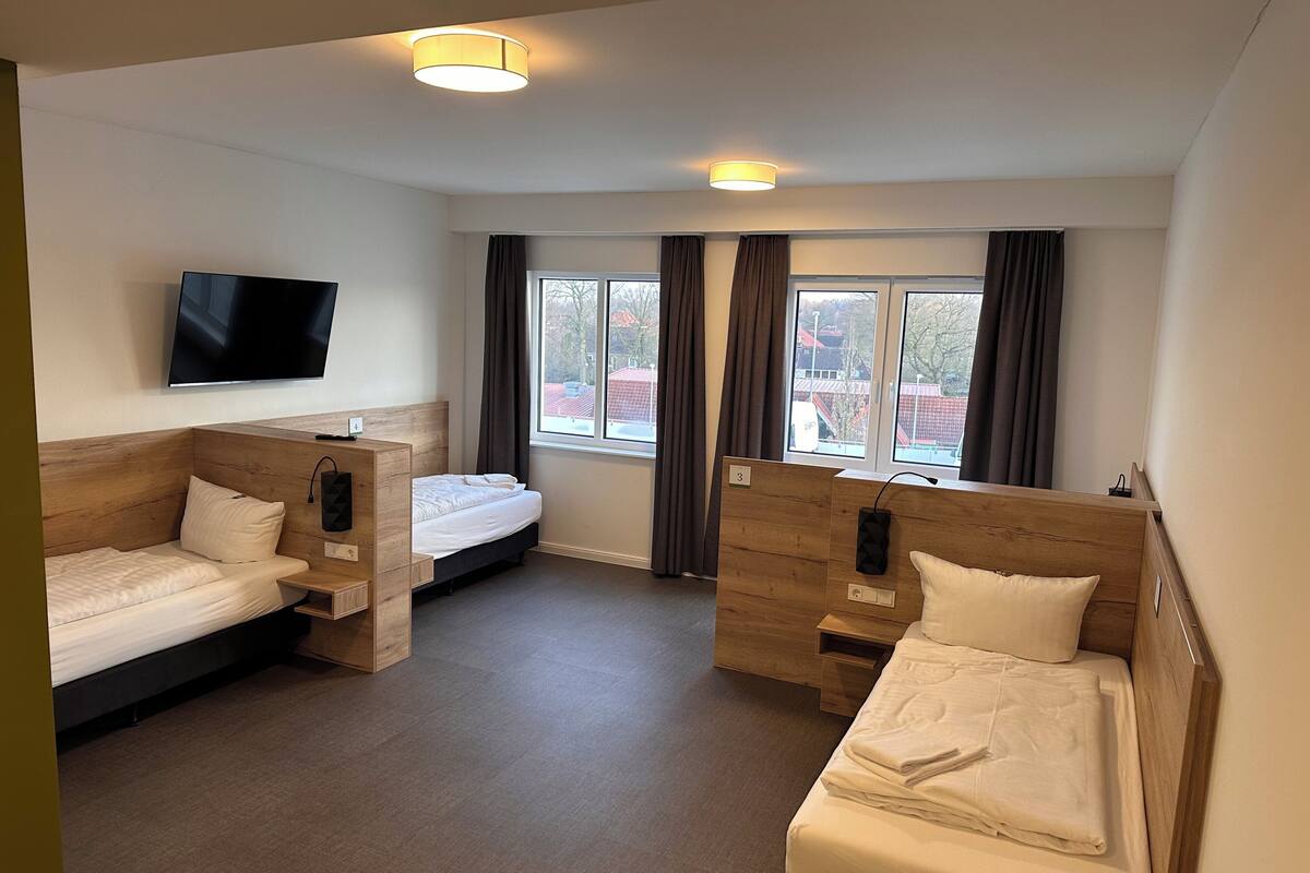 A hotel room with two beds, a TV, a window with curtains, and a wooden headboard.