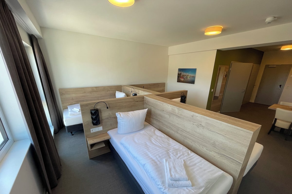 A hotel room with a single bed, a bedside table, a mirror, a small desk, and a window with curtains.