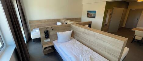 Habitación de hotel con una cama individual, una mesita de noche, un espejo, un escritorio pequeño y una ventana con cortinas.