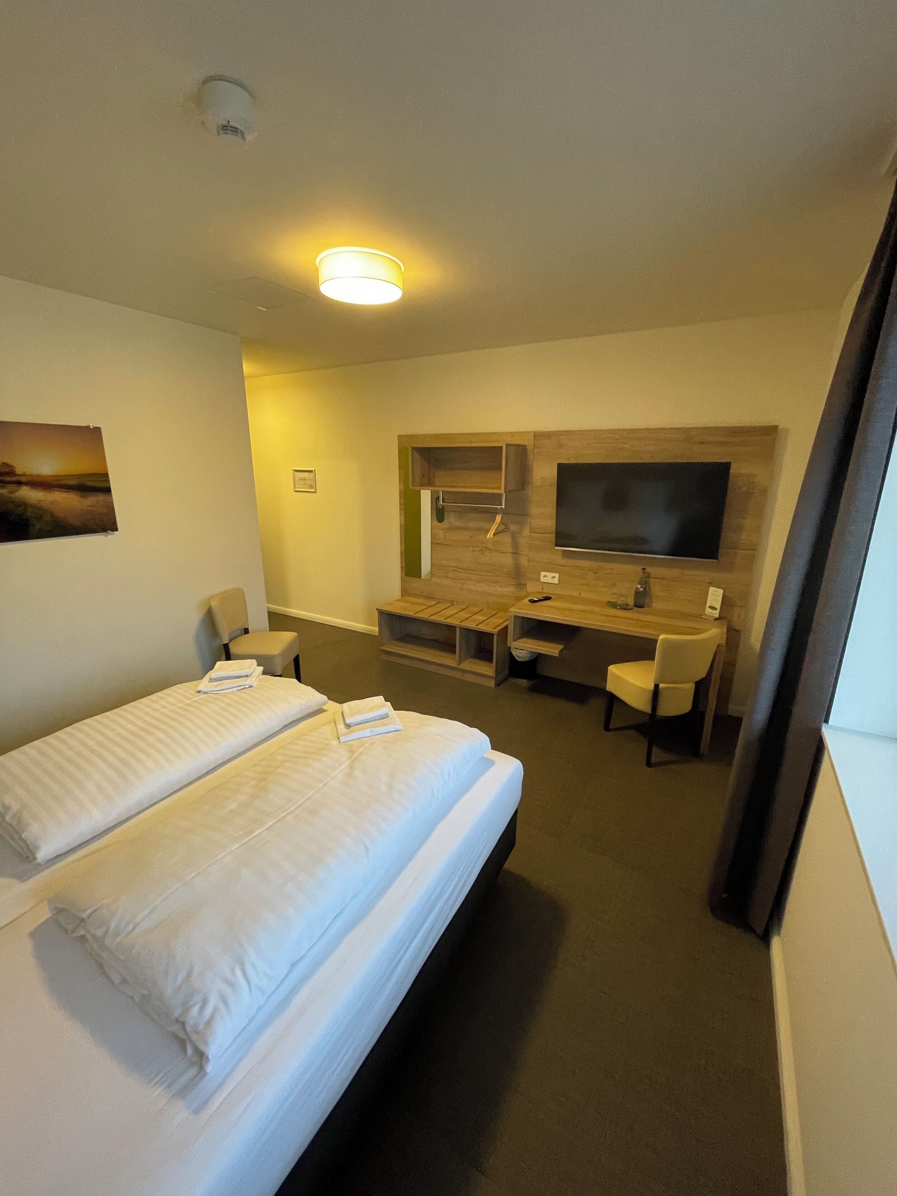 Une chambre d’hôtel avec un lit, un bureau, une chaise, une télévision et un tableau au mur.