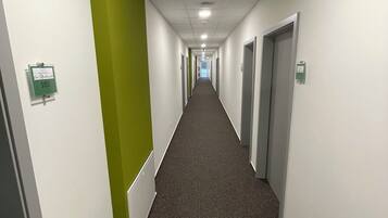 A long, narrow hallway with white walls and a green accent wall on the left. The floor is carpeted, and there are doors on both sides of the hallway.