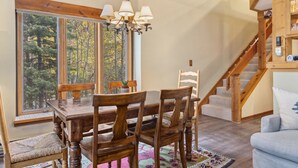 A dining area with a wooden table and chairs, a chandelier, and a large window with a view of trees. - Outpost: Columbine 1024 - Aspens Location! (Wilson)
