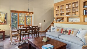 A cozy living room with a dining area, wooden cabinets, and a large window with a view of trees. - Outpost: Columbine 1024 - Aspens Location! (Wilson)