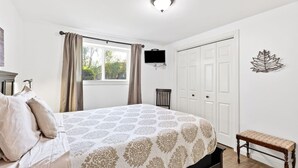 A bedroom with a bed, a bench, a TV, and a door.