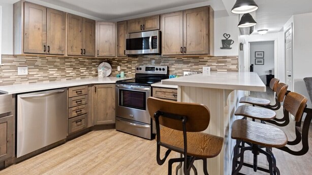 Una cocina moderna con armarios de madera, electrodomésticos de acero inoxidable y una barra desayunadora con taburetes.