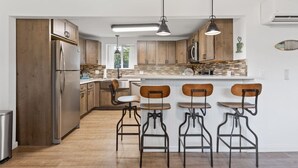 A modern kitchen with wooden cabinets, a stainless steel refrigerator, and bar stools.