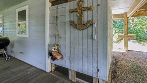 Une porte en bois rustique ornée d’une grande ancre, avec une petite fenêtre et un grillage à l’extérieur.