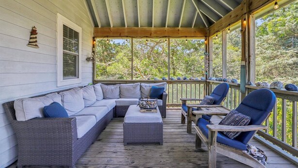Une véranda abritée avec un coin salon doté de coussins, une petite table et une vue sur la verdure environnante.