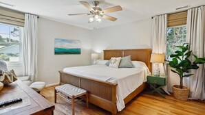 Une chambre à coucher avec un lit en bois, un ventilateur de plafond, une table de chevet avec une lampe, une plante et un tableau au mur.