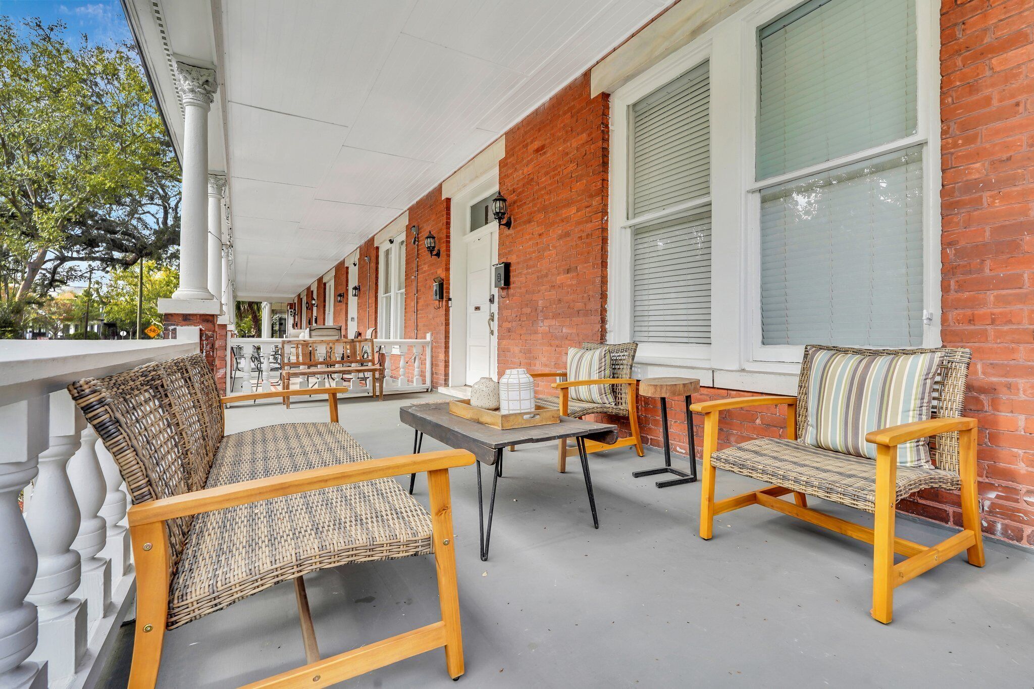 A covered outdoor seating area with wicker furniture and a brick wall.