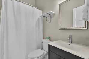 Une salle de bain avec des toilettes blanches, un lavabo, un miroir et un rideau de douche.