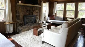 A cozy living room with a stone fireplace, a white sofa, a wooden coffee table, and a ceiling fan.