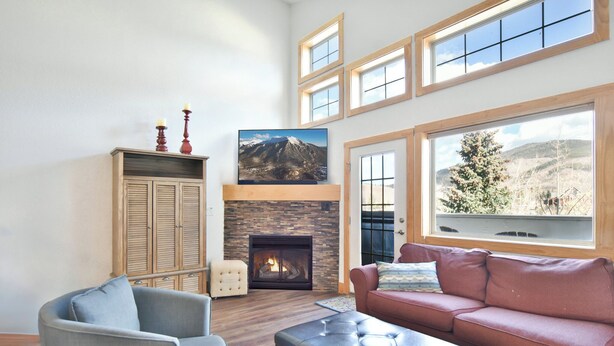 A living room with a fireplace, a large window, and a mountain view. - La Riva Del Lago Condo: Downtown, Close to Everything! (Dillon)