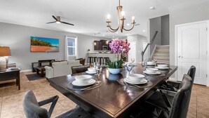 A spacious dining area with a long table set for six, a chandelier, and a view of the kitchen in the background. - Upstay - 23-guest Mansion w Pool Game Room and BBQ (Davenport)