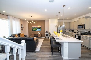 Een moderne keuken met een centraal eiland, een eetgedeelte met een lange tafel, en een woonkamer met een zwarte leren bank.