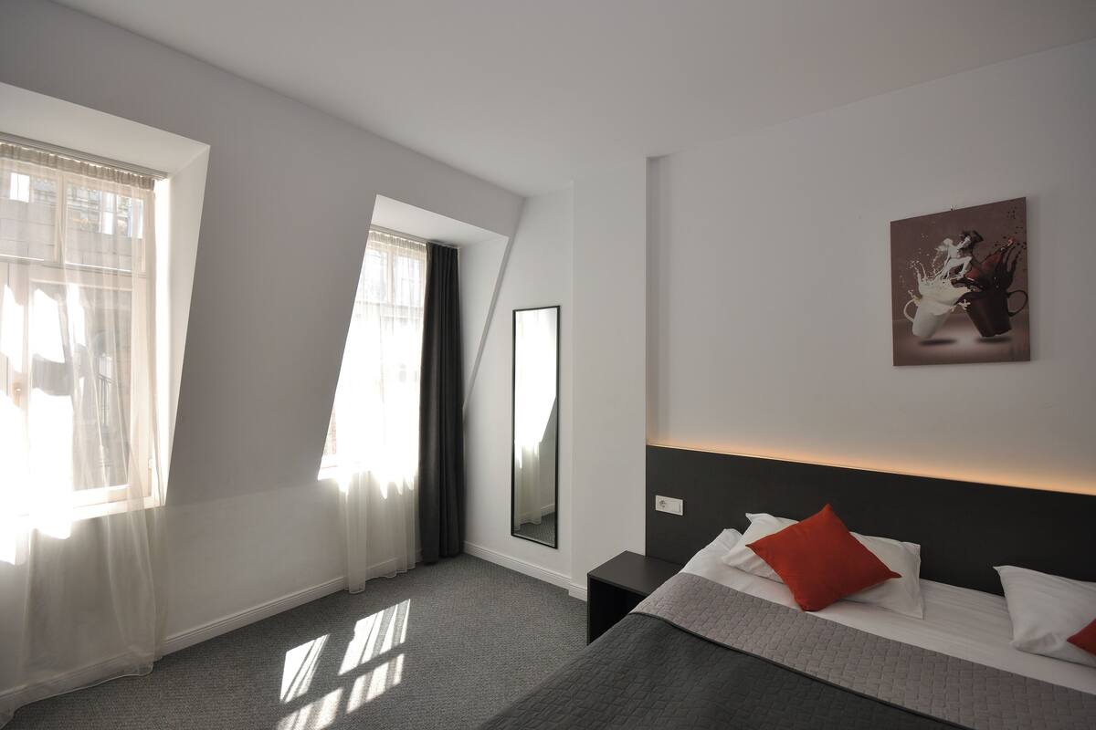 A modern hotel room with a large bed, a bedside table, a mirror, and a painting on the wall.
