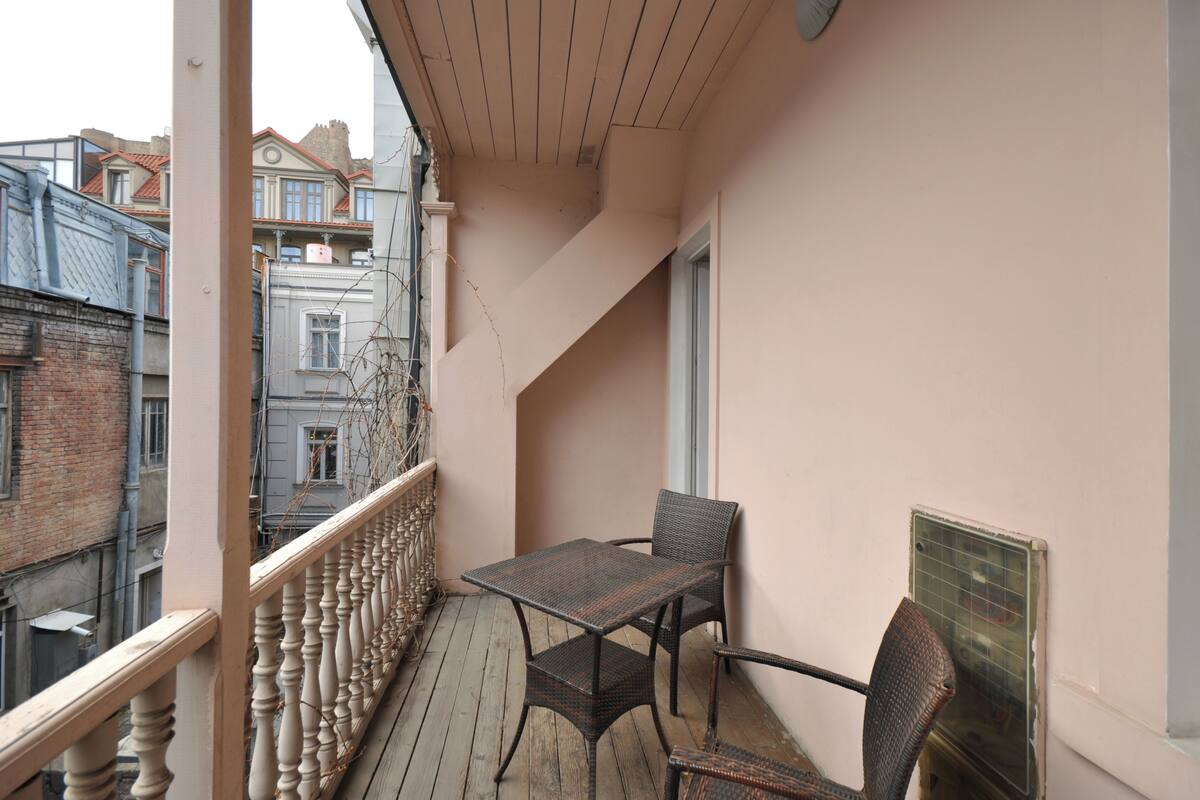 A balcony with a table and chairs, a wooden railing, and a view of neighboring buildings.