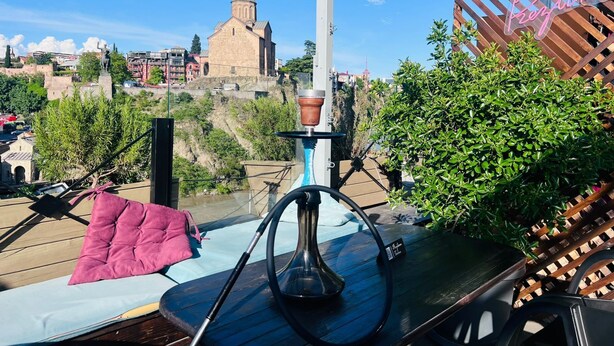 A balcony with a hookah, a pink cushion, and a view of a historic church. - Meidan Inn (Tbilisi)