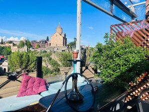 A balcony with a hookah, a pink cushion, and a view of a historic church.