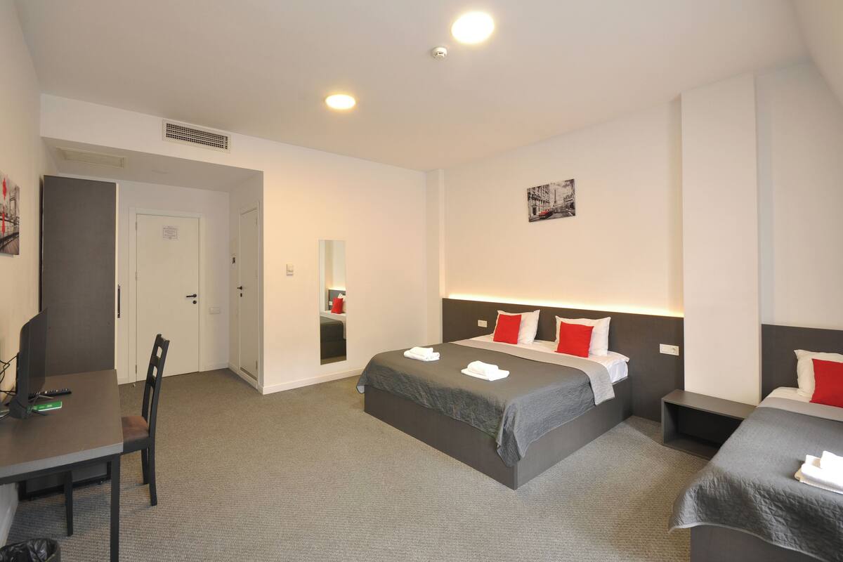 A hotel room with a bed, bedside tables, a desk with a chair, and a mirror.