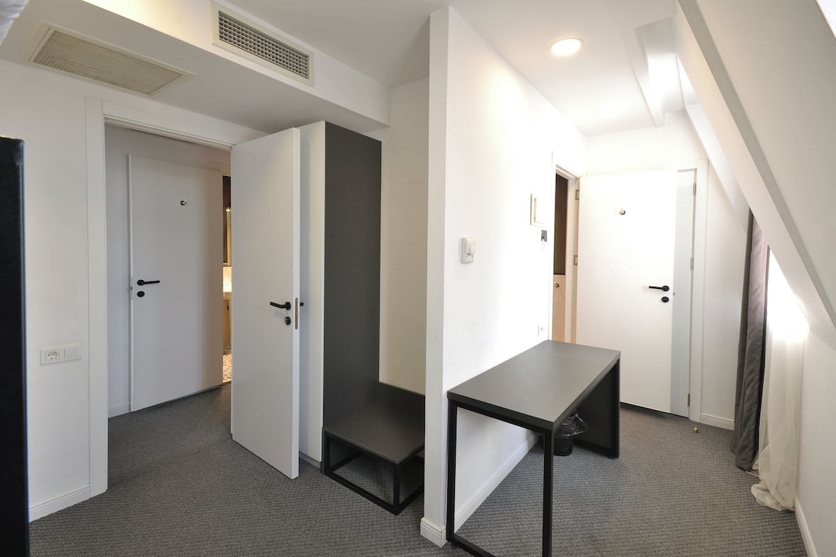 A modern, compact room with a built-in bench, white doors, and a sloped ceiling with a vent.
