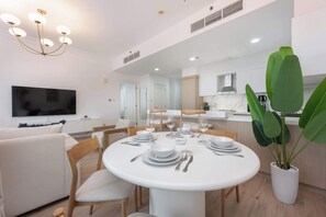 Een moderne eetruimte met een ronde tafel voor vier personen, een flatscreen televisie aan de wand en een potplant in de hoek.