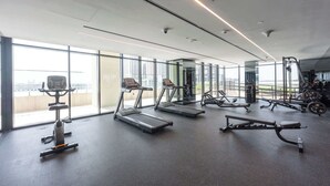 Une salle de sport moderne équipée de tapis de course, d’appareils de musculation et offrant une vue sur la ville grâce à de grandes fenêtres.