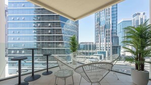 Un balcon agrémenté de chaises modernes, d’une petite table et d’un pot de fleurs, offrant une vue sur un paysage urbain dominé par de hauts immeubles.