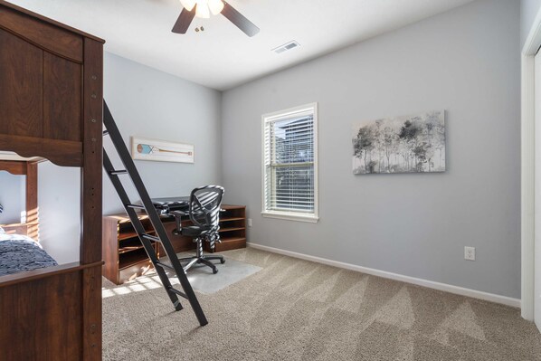 A bedroom with a bed, desk, chair, ladder, and artwork on the wall.