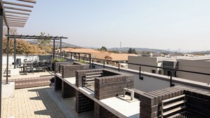 Eine Dachterrasse mit Außenbestuhlung, einer Pergola und Blick auf die Skyline der Stadt.