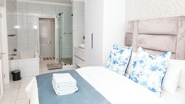 Ein modernes Schlafzimmer mit einem ordentlich bezogenen Bett, einer Duschkabine und einem Badezimmer mit Badewanne und Toilette.