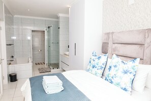 Quarto moderno com cama bem arrumada, chuveiro em box de vidro e banheiro com banheira e vaso sanitário.