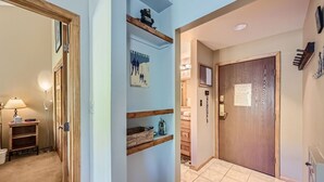 A hallway with a wooden door, a shelf with a poster, and a lamp. - 1147 Flying Dutchman 1 Bedroom Condo (Keystone)