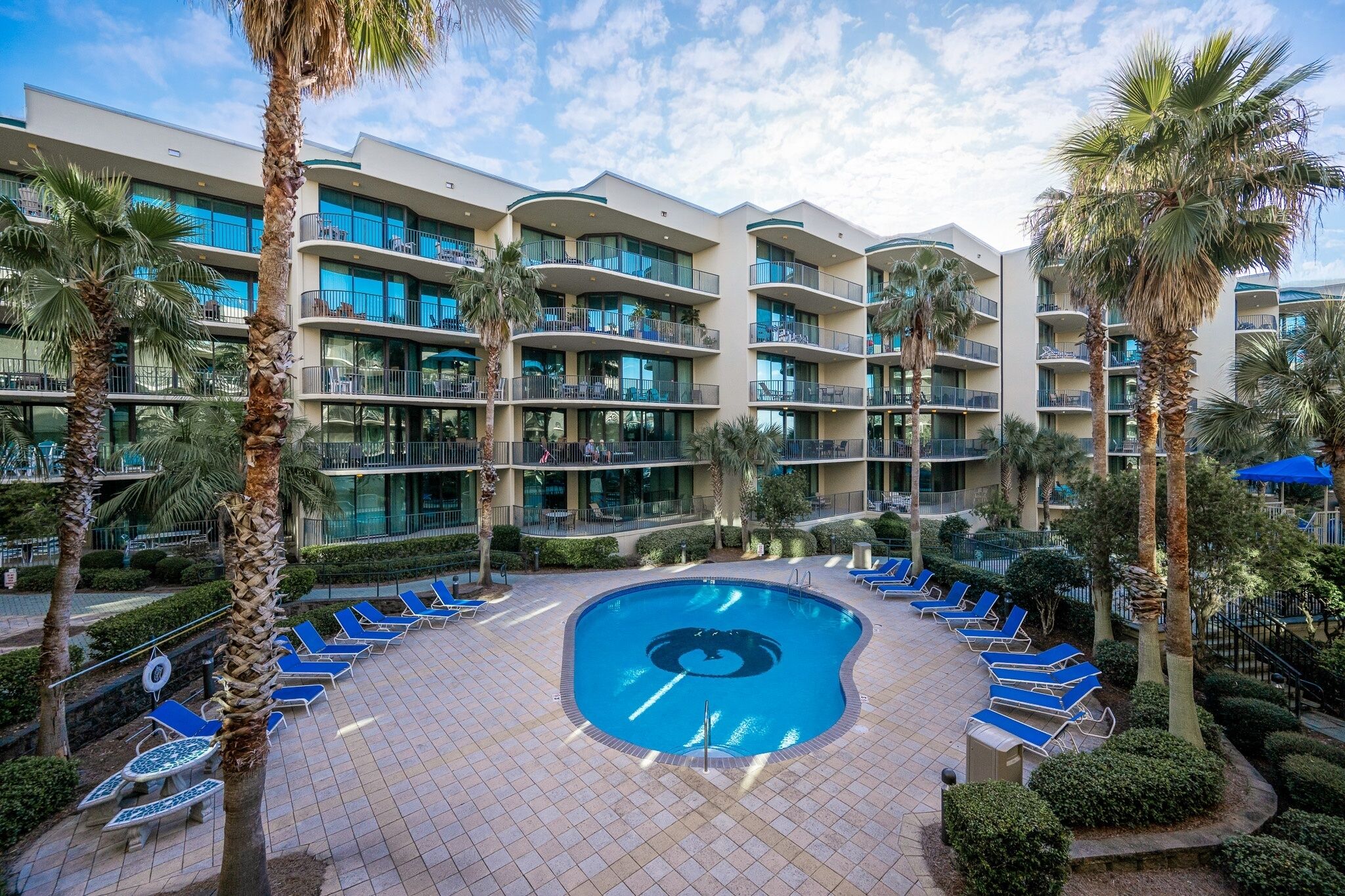 Et hotel med swimmingpool omgivet af liggestole og palmer.