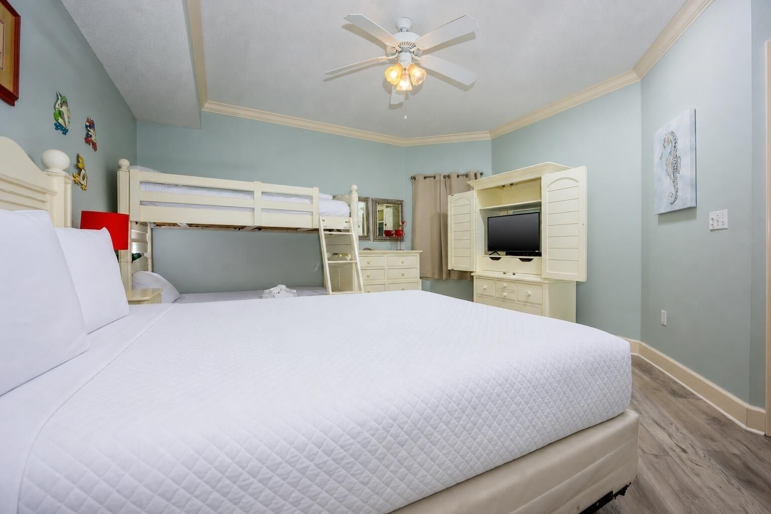 Een slaapkamer met een stapelbed, een bureau, een televisie en een plafondventilator.