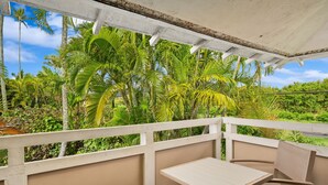 A covered outdoor seating area with a table and chairs, surrounded by lush greenery and palm trees. - Kauai Plantation Hale Suites E12 1 Bedroom Condo (Kapaa)