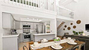 Una cocina moderna con electrodomésticos de acero inoxidable, un comedor con una mesa de madera dispuesta para cuatro personas y un sofá gris en la sala de estar.