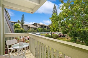 A balcony with a white table and chair, overlooking a residential street with houses and parked cars. - Kauai Puamana 4b 2 Bedroom Condo (Princeville)