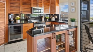A modern kitchen with wooden cabinetry, a central island, stainless steel appliances, and pendant lighting. - Wailea Ekolu 104 2 Bedroom Condo (Kihei)