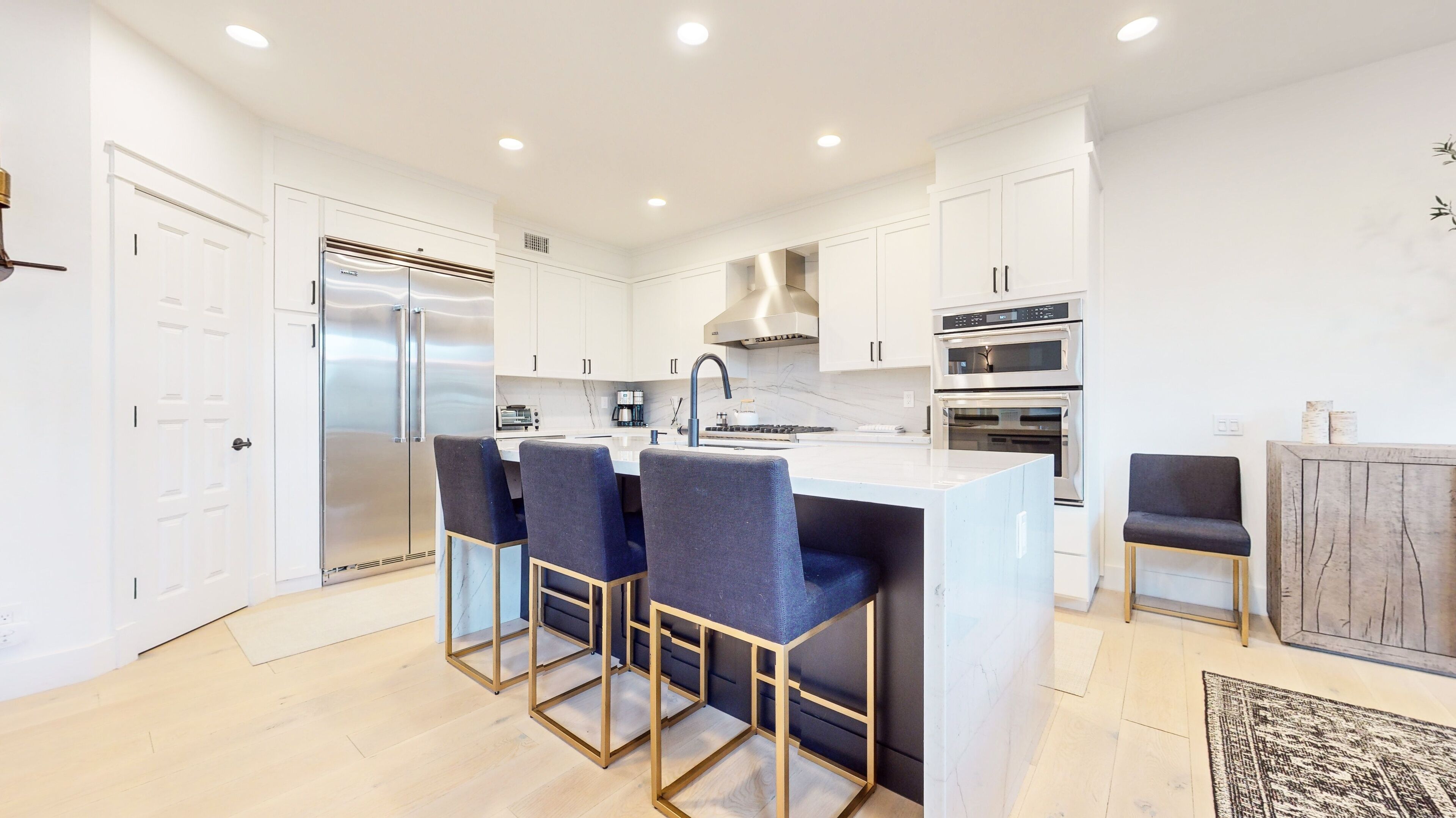 A modern kitchen with white cabinetry, stainless steel appliances, and a central island with bar stools.