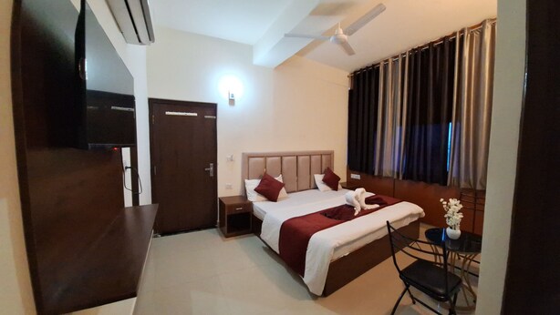 Une chambre d’hôtel comprenant un lit, une chaise, une petite table avec un vase, un ventilateur de plafond et un appareil de climatisation.
