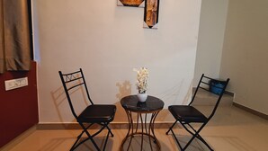 Une petite pièce avec deux chaises noires et une table ronde sur laquelle est posé un vase de fleurs blanches.